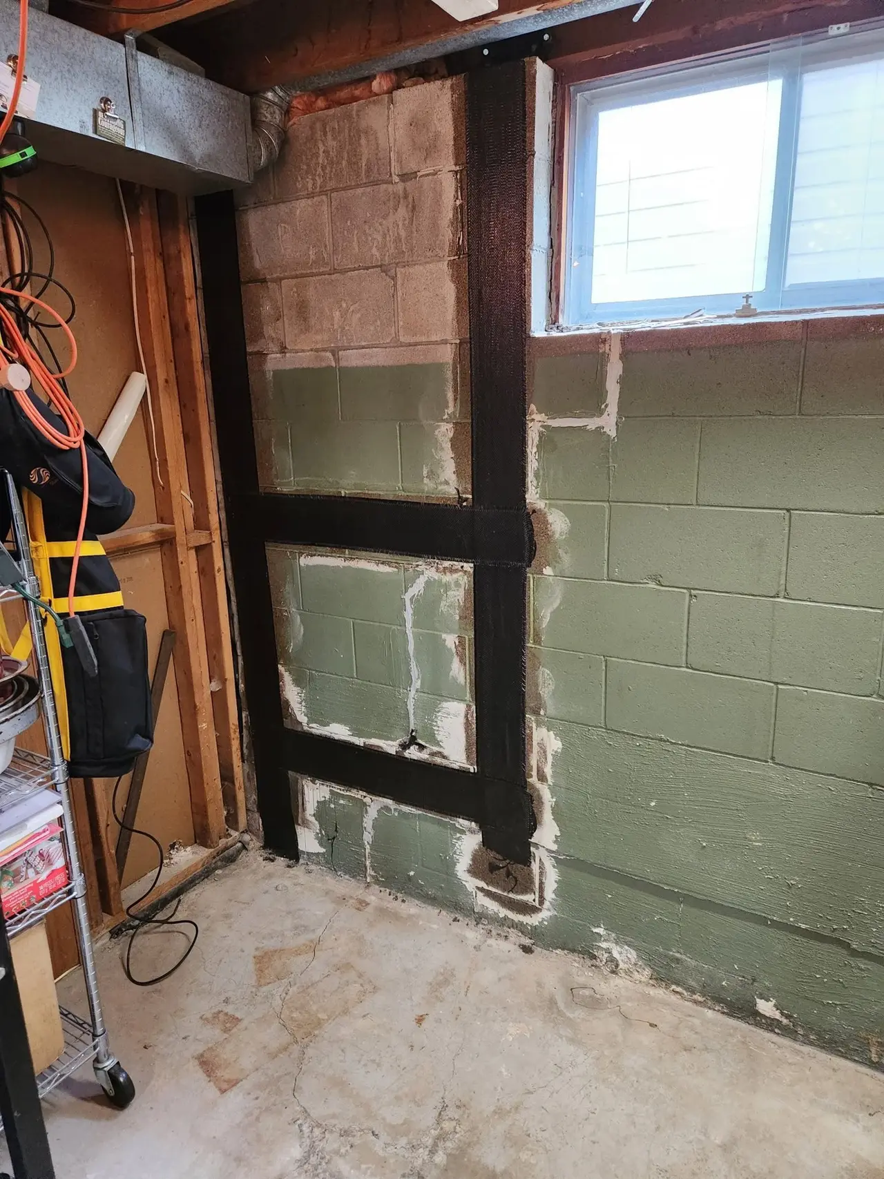 Steel beams bracing a bowed block basement wall below a window