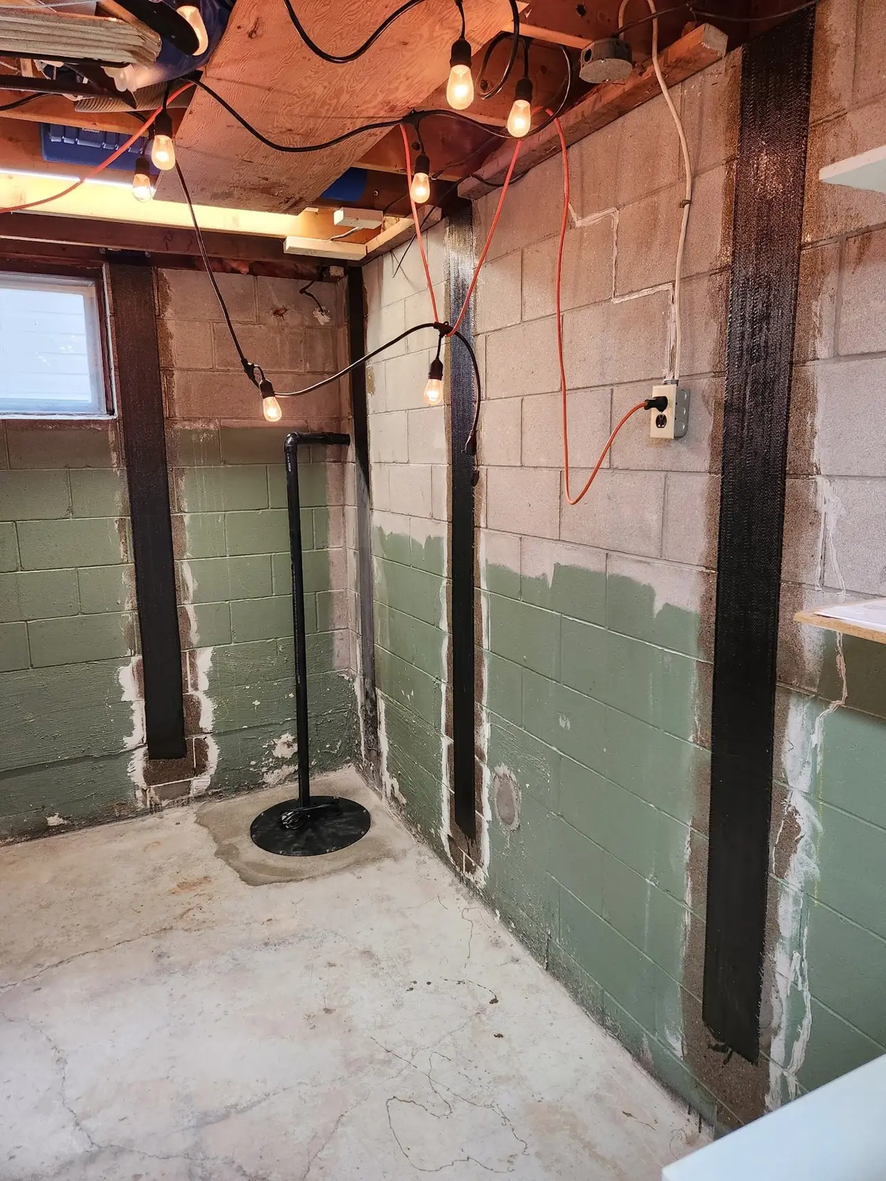 Vertical steel braces on a block basement wall, with a sump pit in the corner