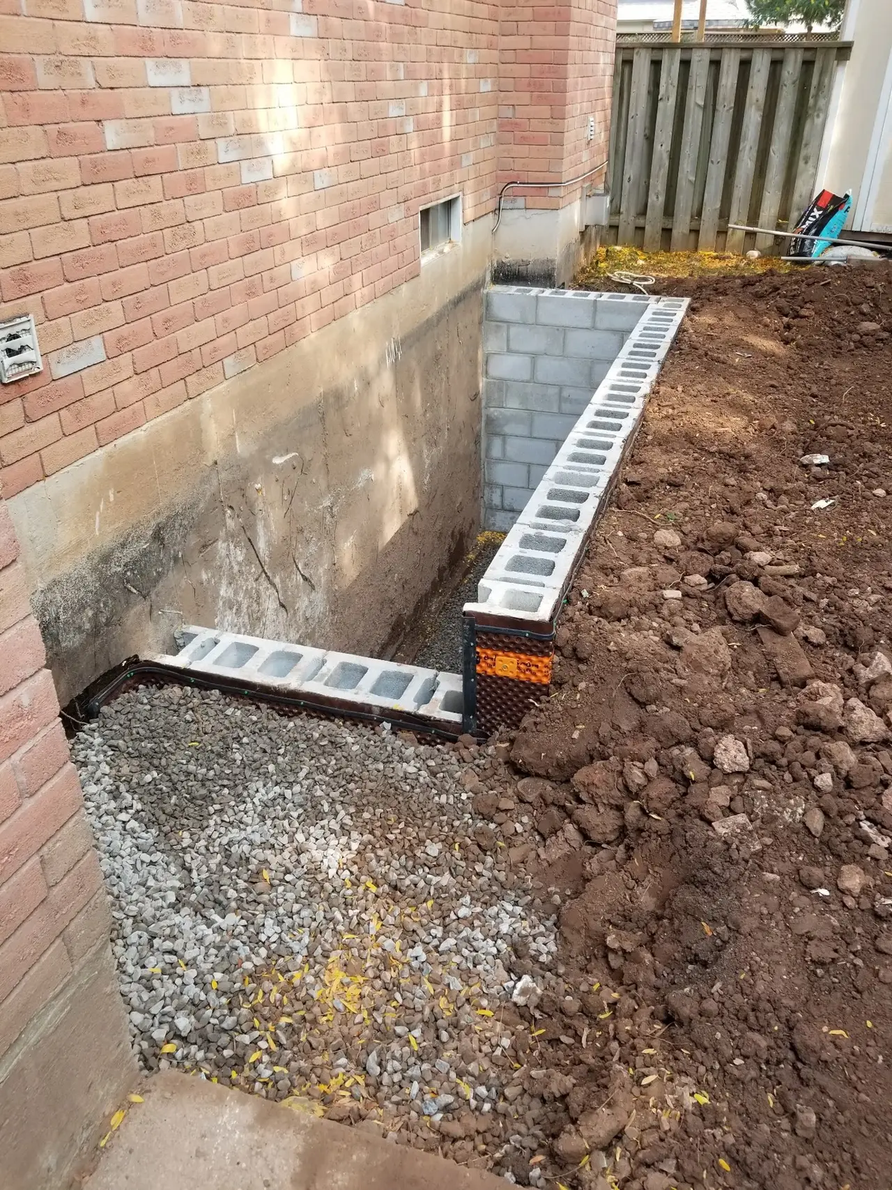 Exterior foundation excavation beside a brick house with new weeping tile and drainage stone