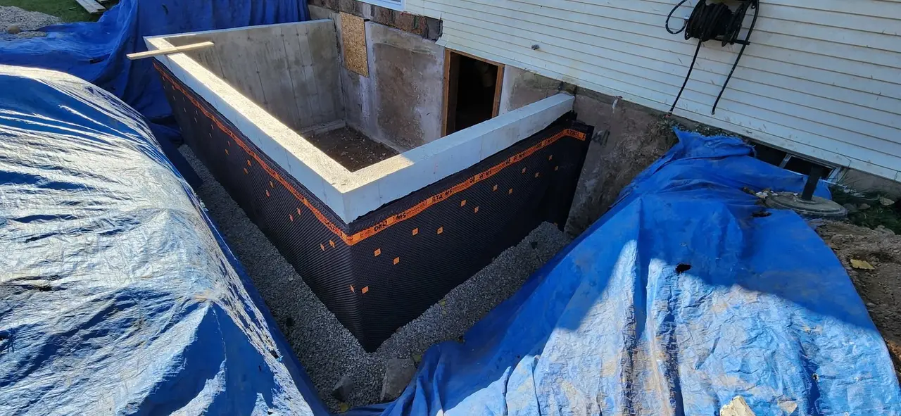 New poured foundation for an addition, wrapped in drainage membrane beside the house