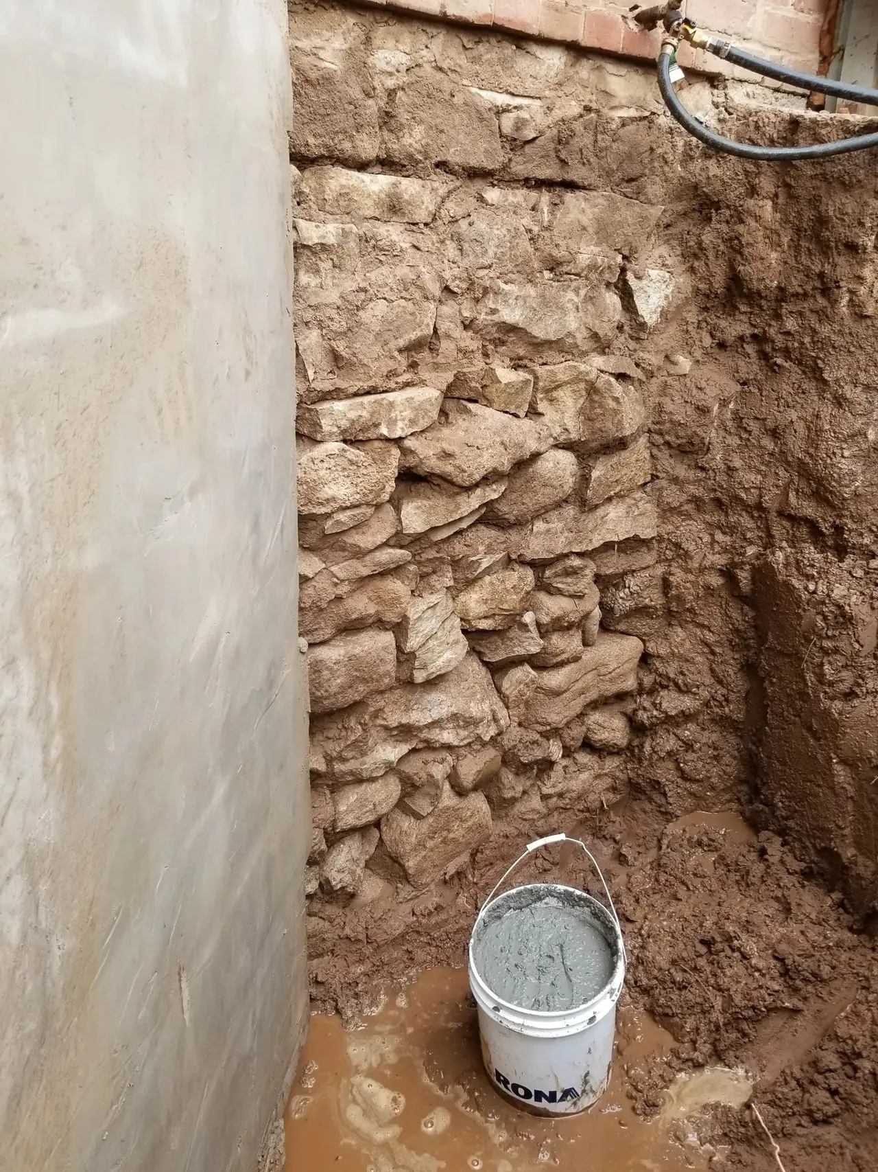 Old stone foundation wall exposed in an excavation beside a house