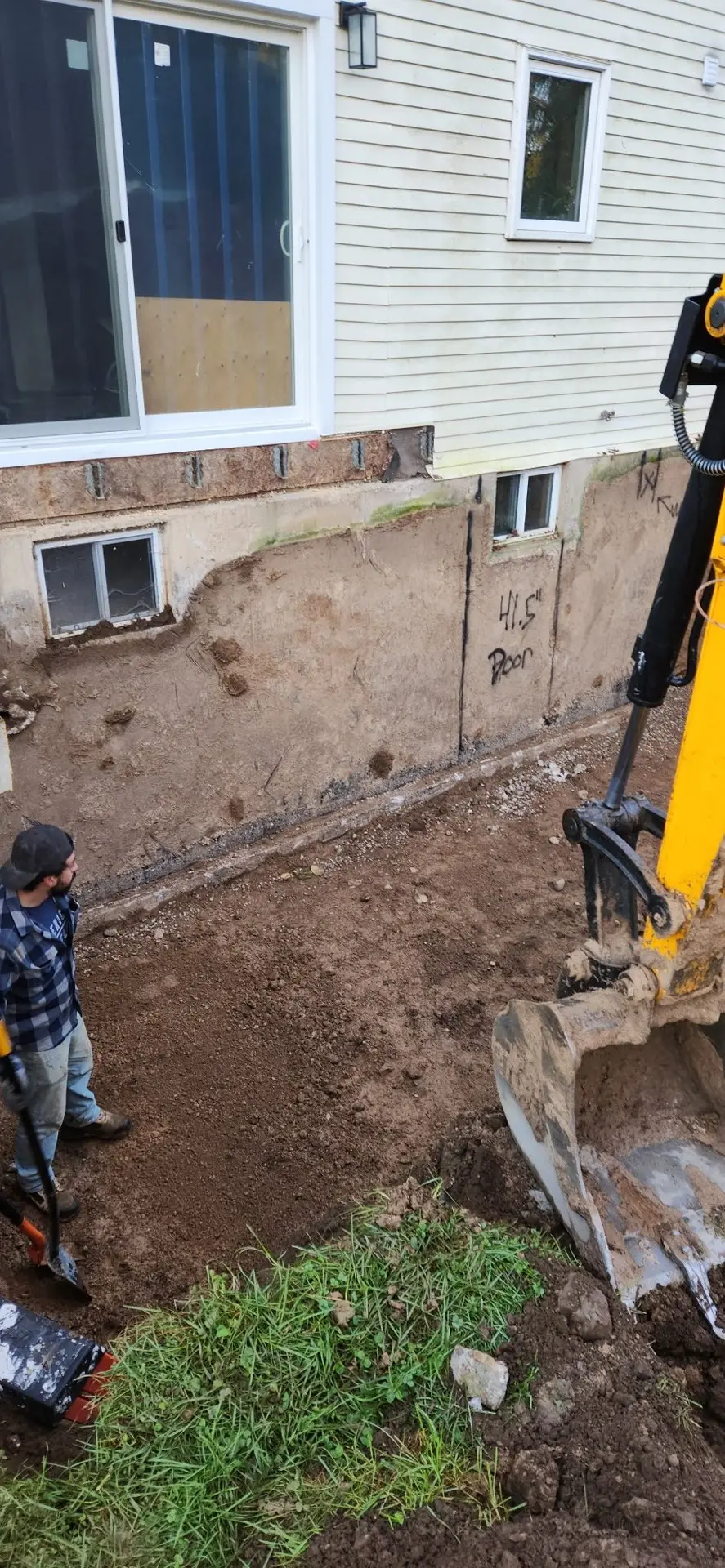Excavation along a house foundation for exterior repair, with a backhoe on site