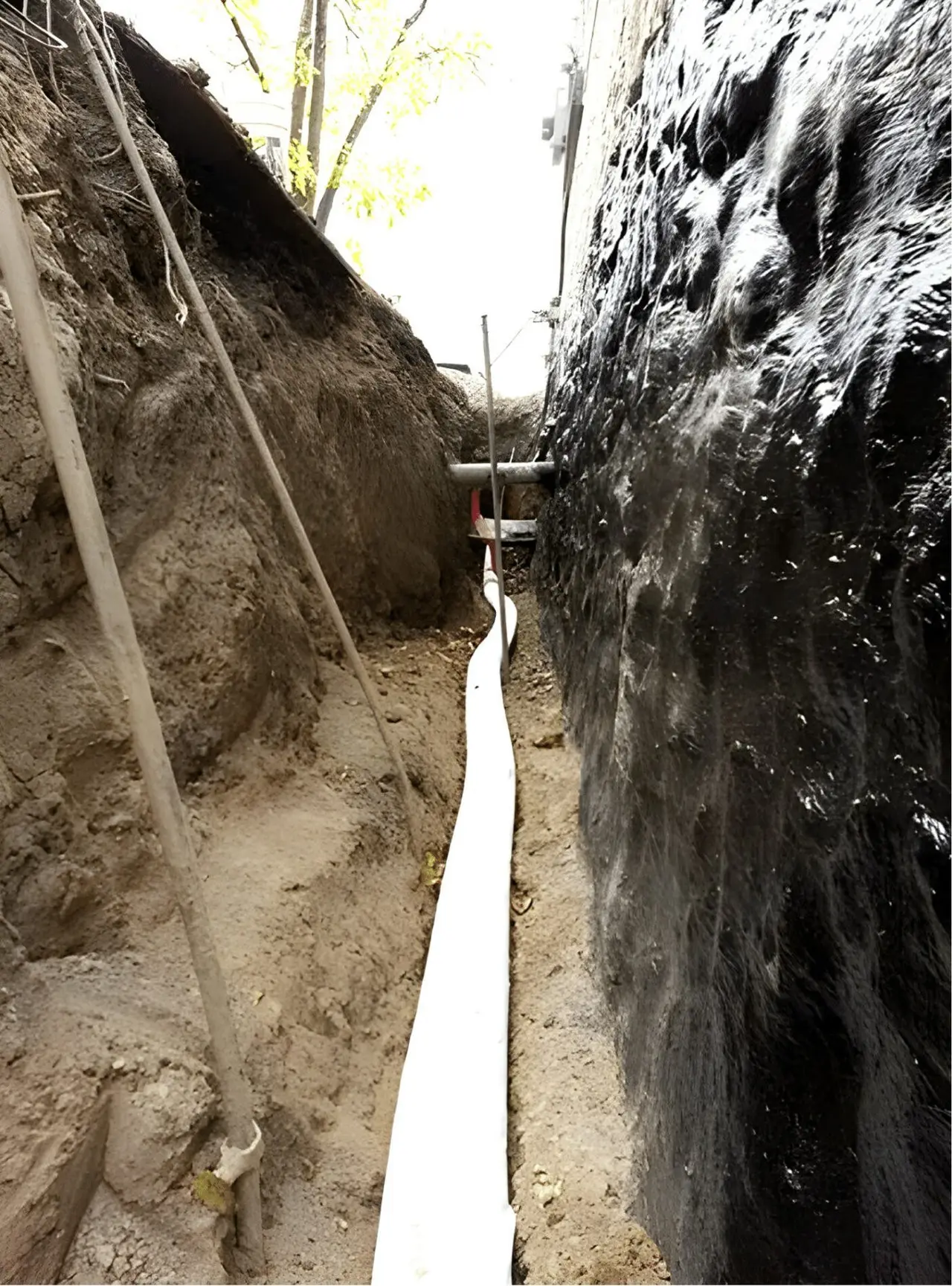 Hand-dug trench along a foundation wall with new waterproofing membrane