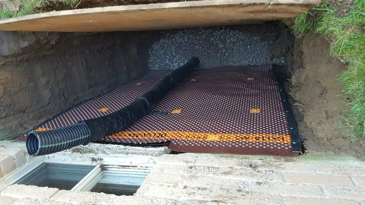Window well drain repair in progress, weeping tile and drainage stone exposed
