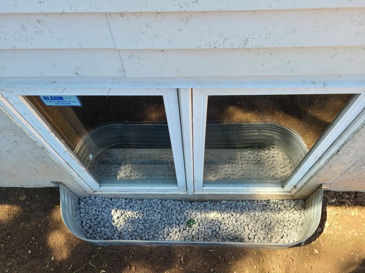 New galvanized window well with drainage stone installed against a basement window