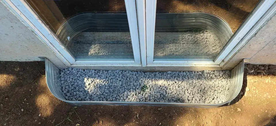 New galvanized window well with drainage stone installed against a basement window
